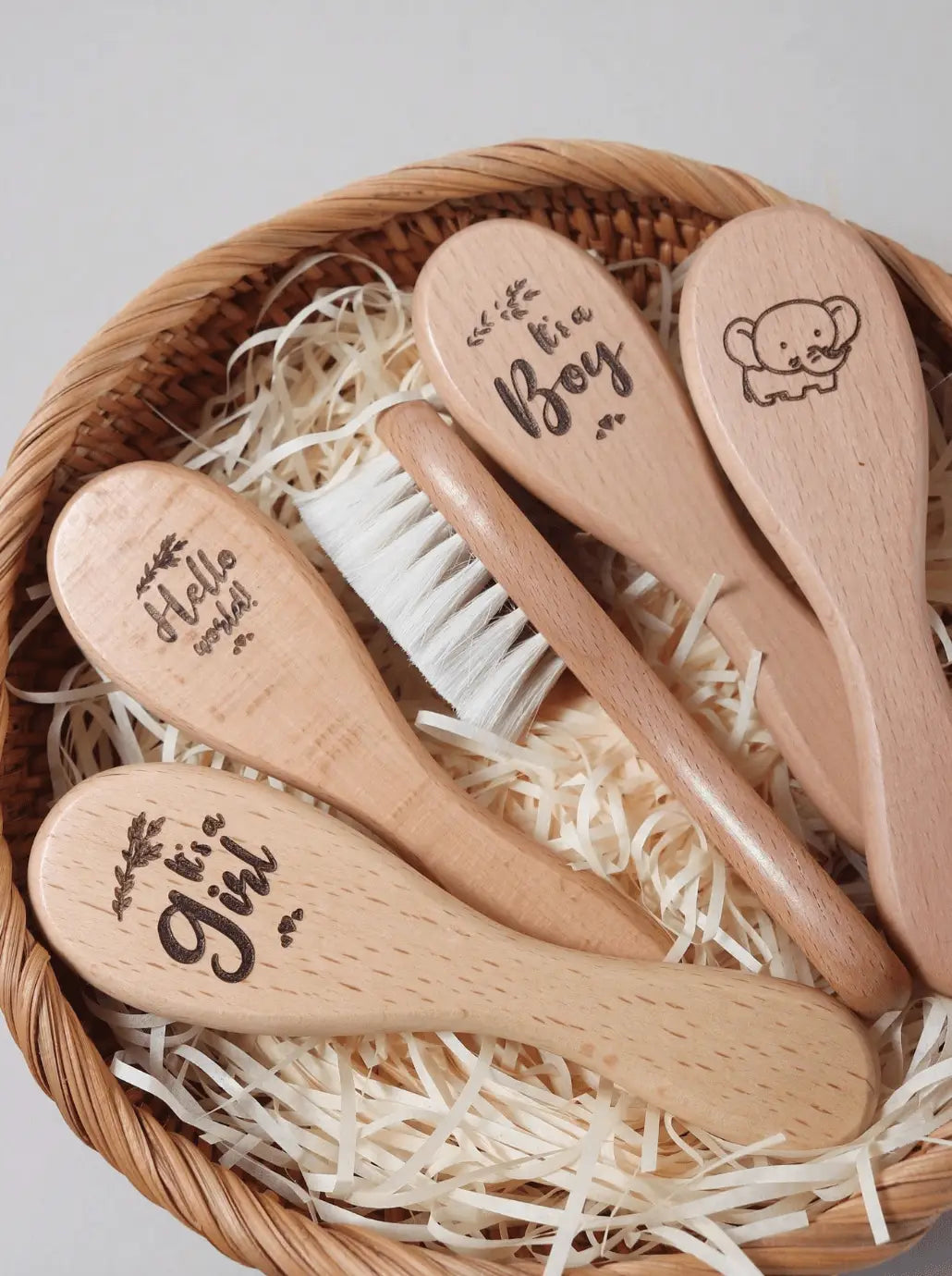 Wooden baby brushes with "Hello," "Boy," and decorative text in woven basket with straw