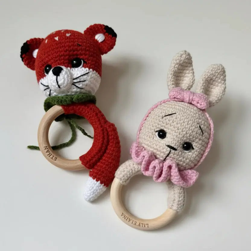 Crocheted fox and bunny baby rattles with wooden rings on white background
