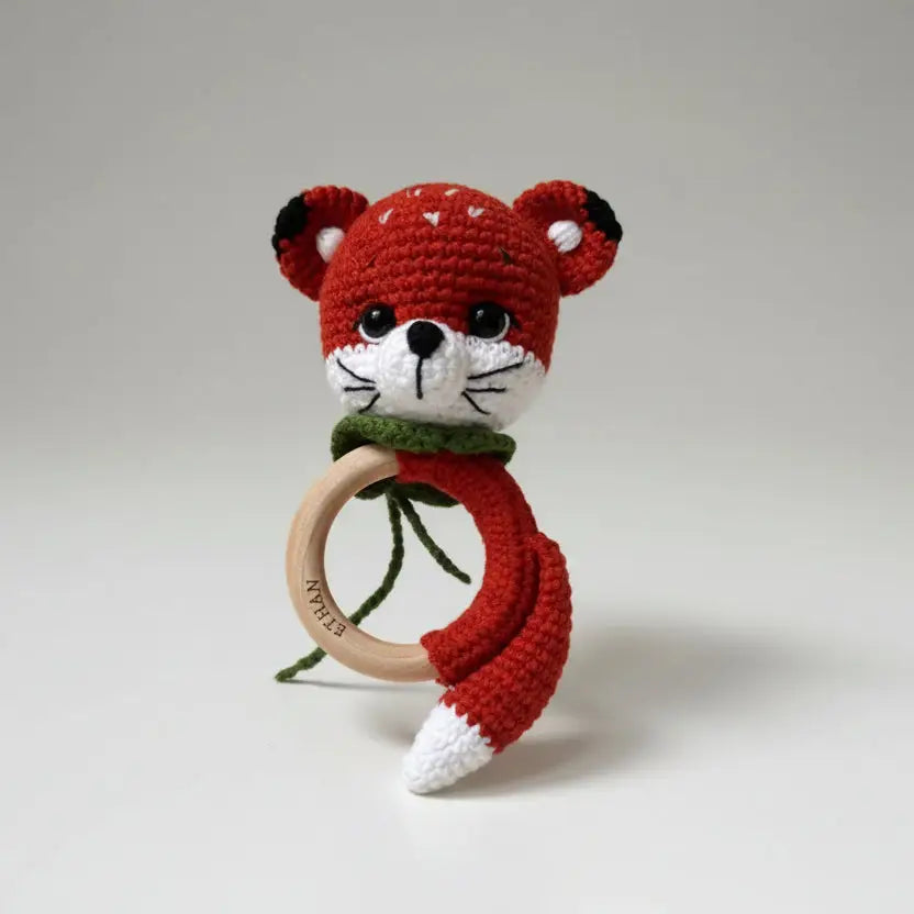 Crocheted red fox baby rattle with wooden teething ring on white background