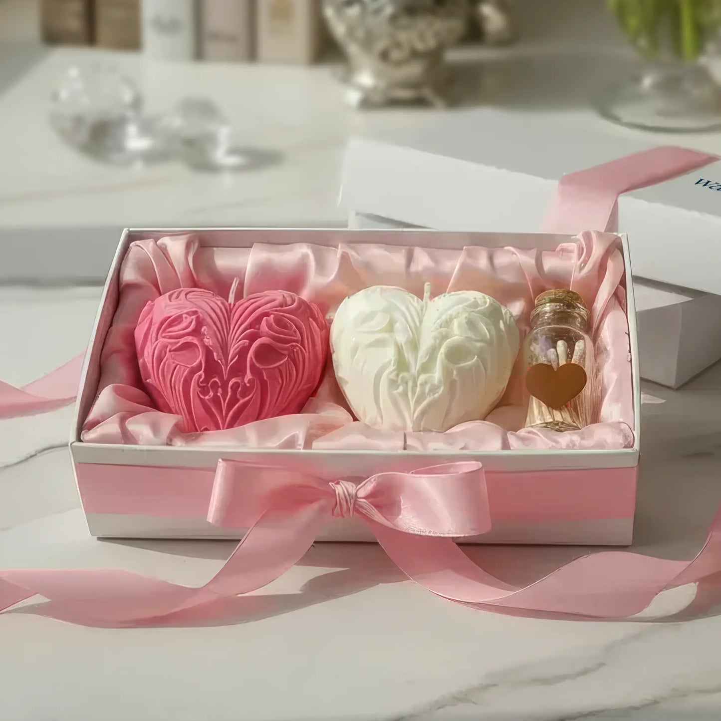 Three heart-shaped candles in a decorative box with pink ribbon on a table.