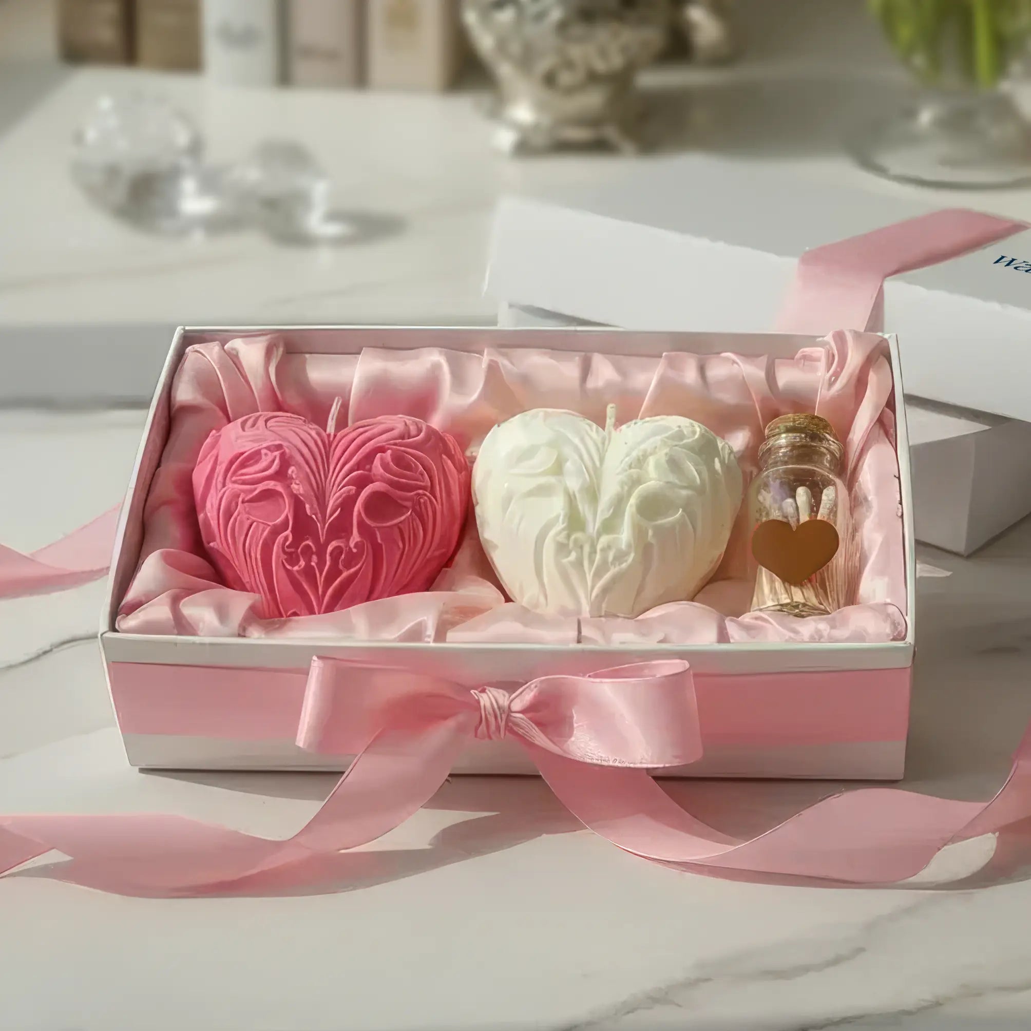 Three heart-shaped candles in a decorative box with pink ribbon on a table.