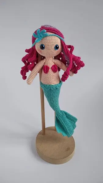 a crocheted mermaid doll on a wooden stand