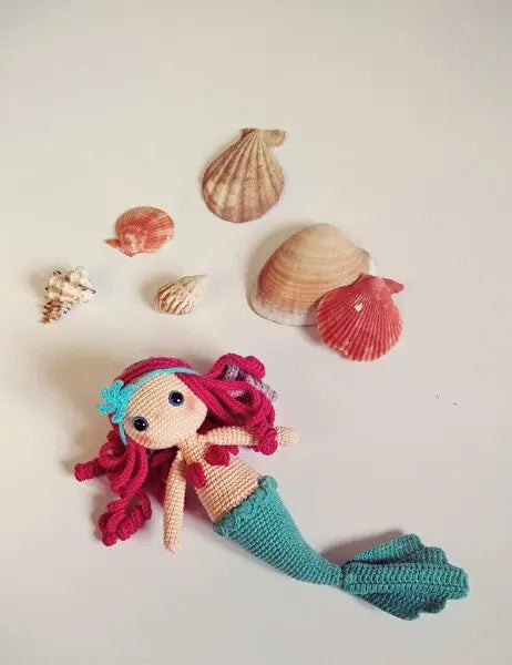 a crocheted mermaid doll surrounded by seashells