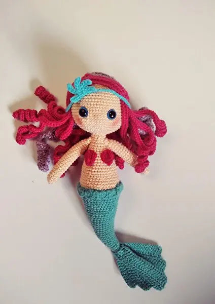 a crocheted mermaid doll laying on a white surface