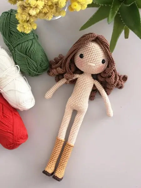 a crocheted doll next to two skeins of yarn