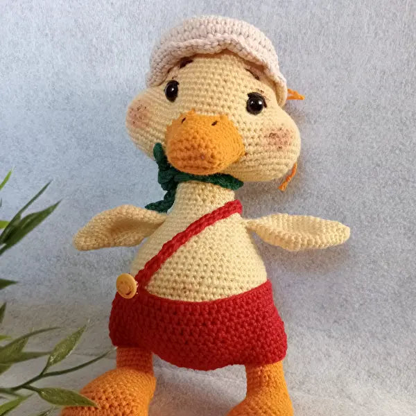 a crocheted ducky doll next to a plant