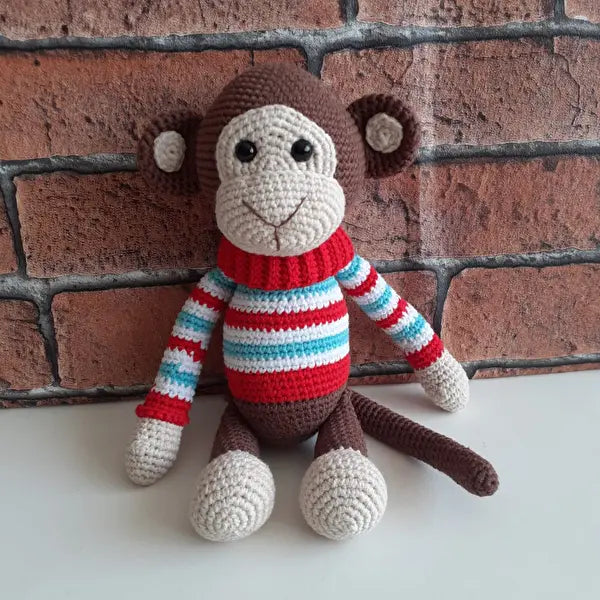 a crocheted monkey sitting next to a brick wall