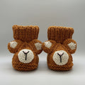 Knitted baby booties with bear faces, brown with white accents, on pink background