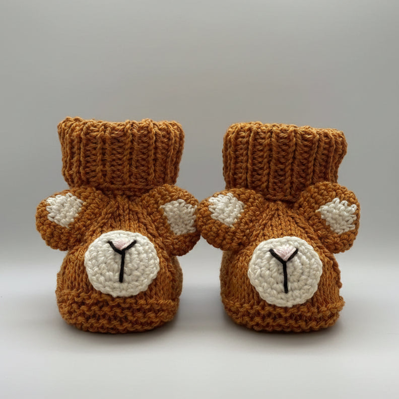 Knitted baby booties with bear faces, brown with white accents, on pink background
