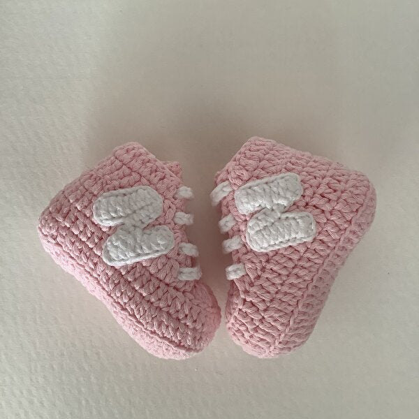 Handmade pink crochet baby booties with white decorative stitching, soft and cozy.