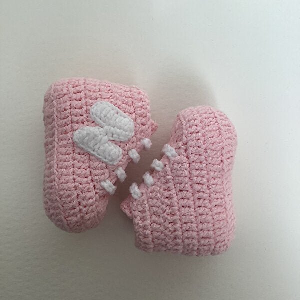 Pink crocheted baby booties with white decorative stitching on a light background