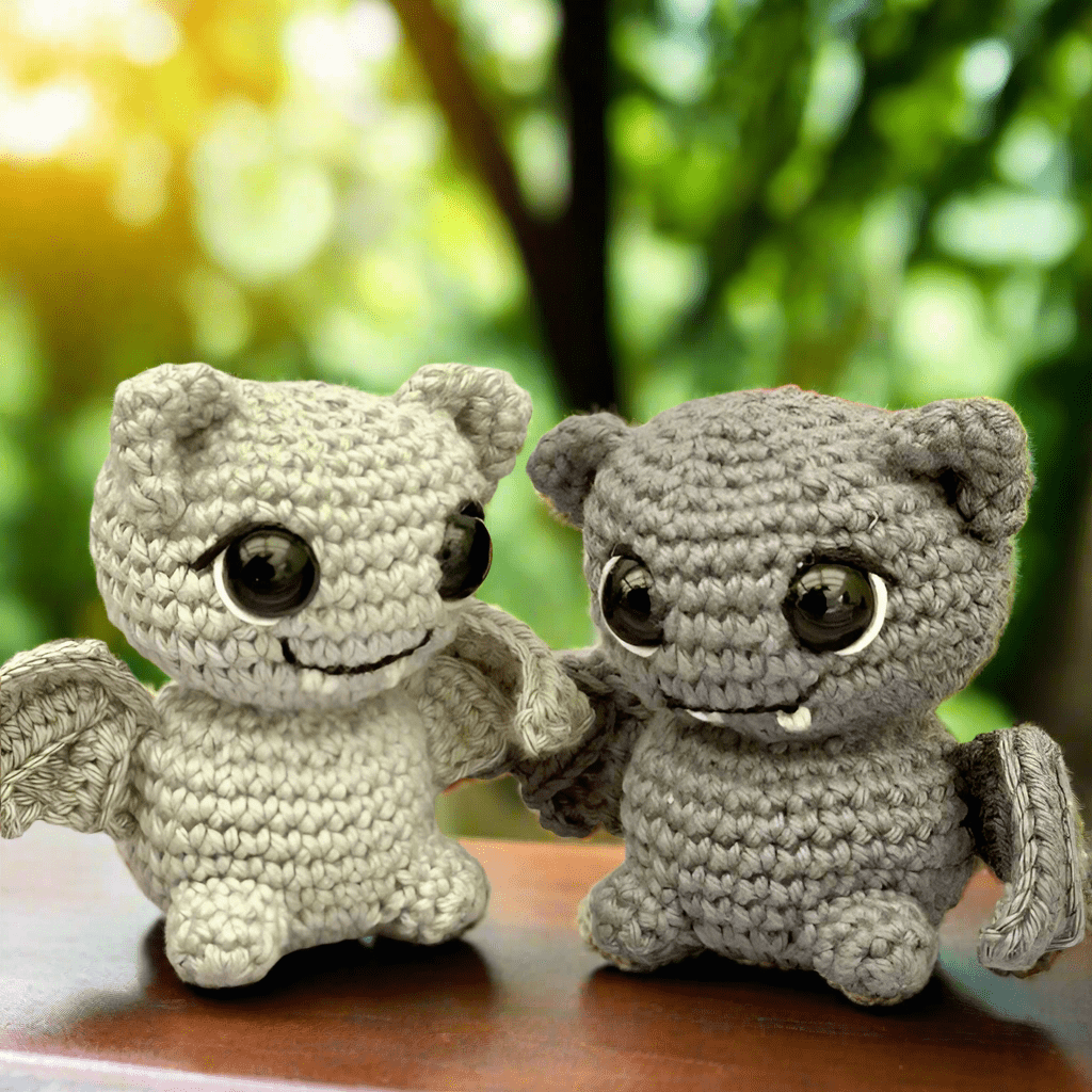 Two crochet creatures with big eyes sitting together, smiling on a blurry green background