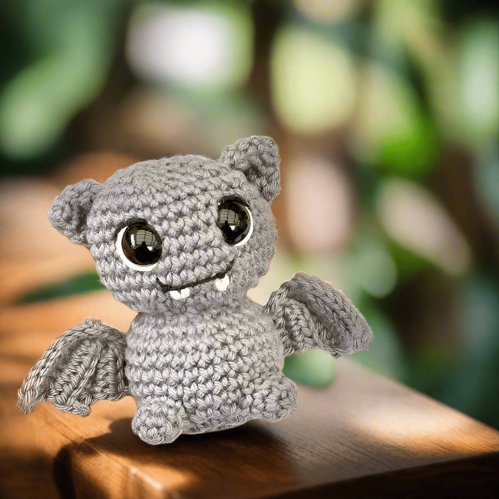 Crocheted gray bat with big eyes sitting on a wooden surface, smiling sweetly