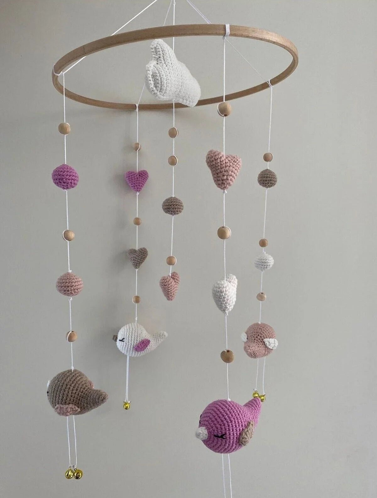 Crocheted baby mobile with birds, hearts, spheres in pink, white, and gray tones