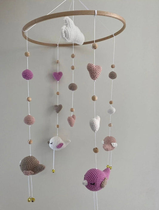 Crocheted baby mobile with birds, hearts, spheres in pink, white, and gray tones