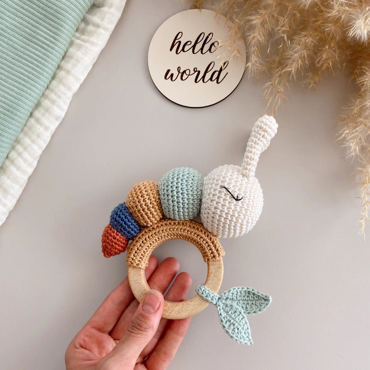 Crocheted bunny teething ring with colorful segments, held by hand near "hello world" sign