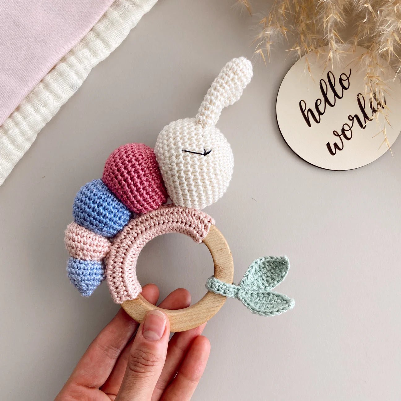 Crocheted bunny teething ring with wooden base, pastel colors, held by a hand