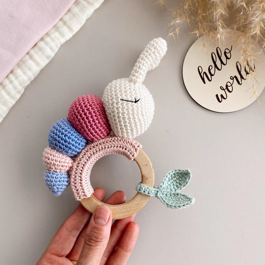 Crocheted bunny teething ring with wooden base, pastel colors, held by a hand