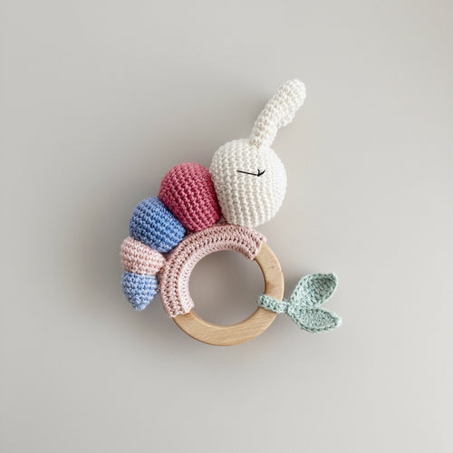 Crocheted bunny teething ring with wooden base, pastel colors, held by a hand