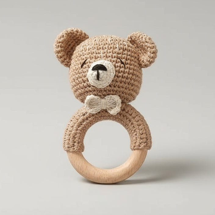 Crocheted teddy bear rattle with wooden teething ring on neutral background