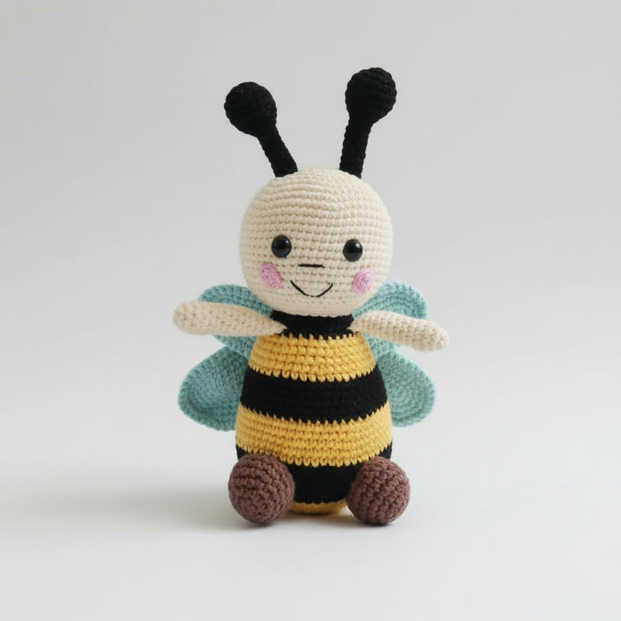 Crocheted bee plushie with smiling face, black antennae, and teal wings