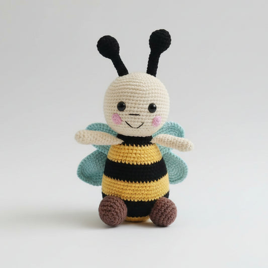 Crocheted bee plushie with smiling face, black antennae, and teal wings