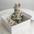 Two crocheted rabbit toys in a white box with gold heart pattern on a white surface.