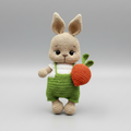 Crocheted bunny in green overalls holding a bright orange carrot