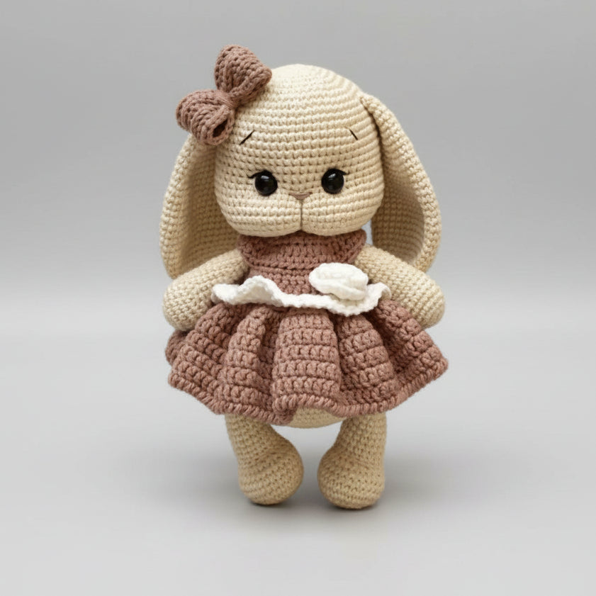 Crocheted bunny doll with floppy ears, wearing a ruffled brown dress and bow