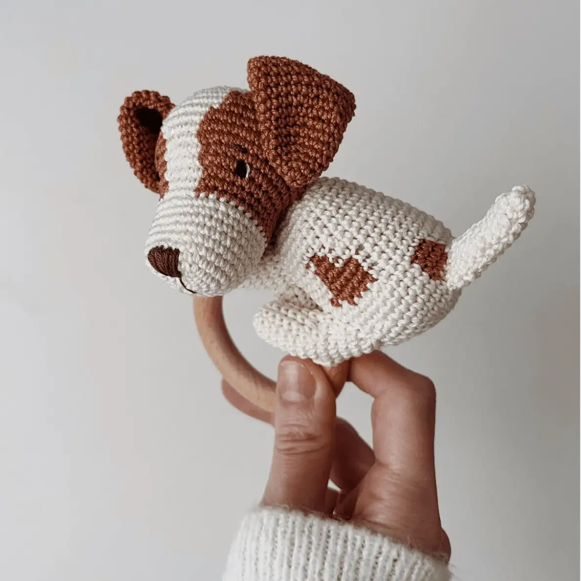 Crocheted brown and white puppy toy with wooden teething ring, held by hand