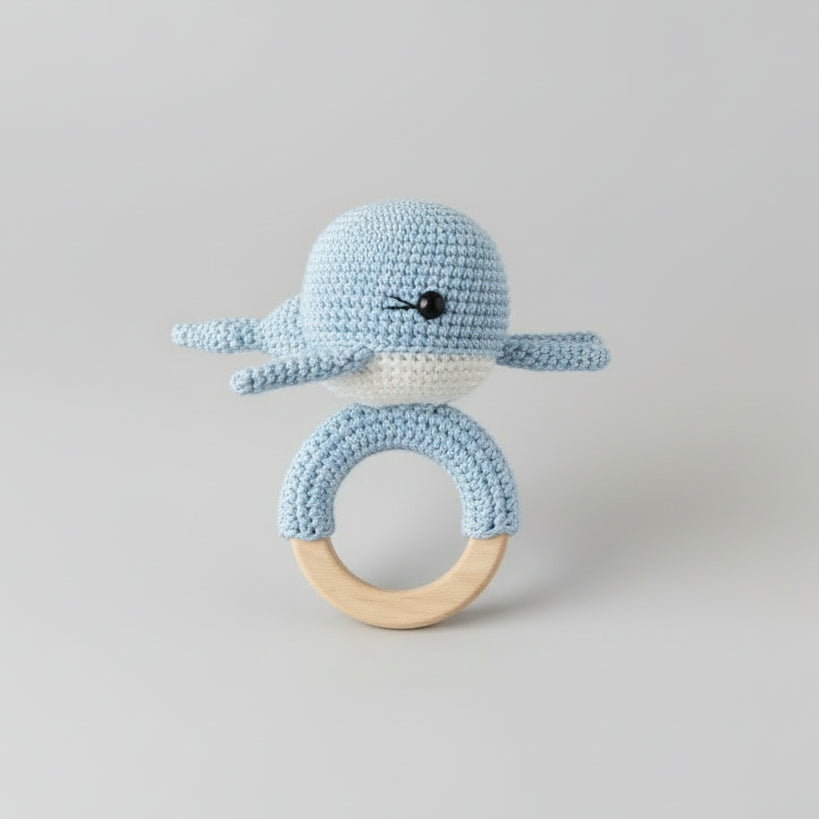 Blue crochet whale baby rattles with wooden rings on fuzzy white background