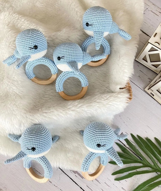 Blue crochet whale baby rattles with wooden rings on fuzzy white background