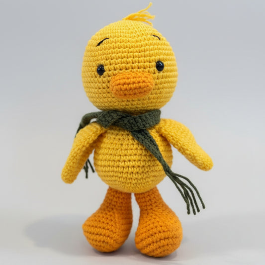 Crocheted yellow duck with green scarf, sitting against a light background