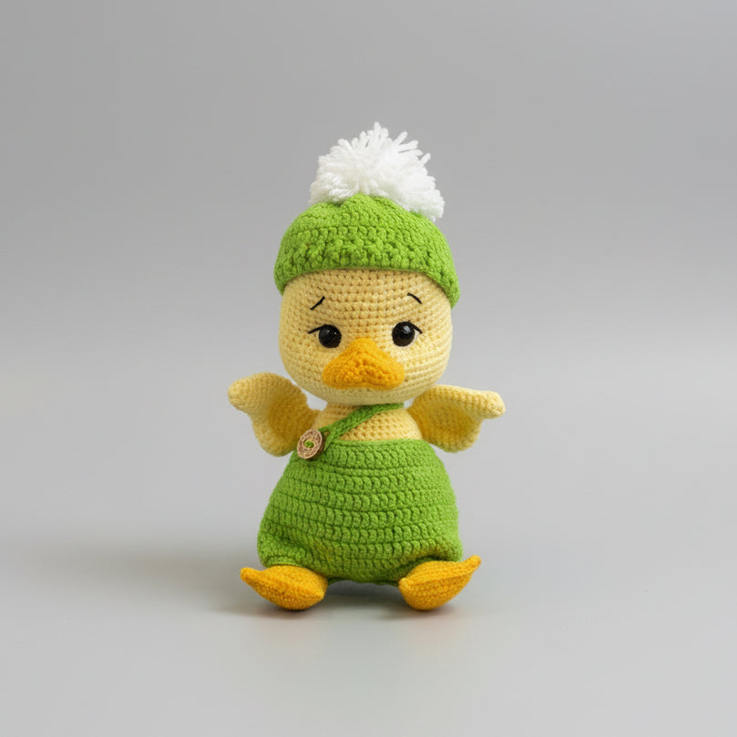 Crocheted baby duck in green outfit with white pom-pom hat, sitting cutely