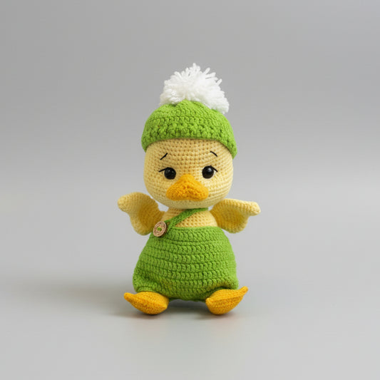Crocheted baby duck in green outfit with white pom-pom hat, sitting cutely