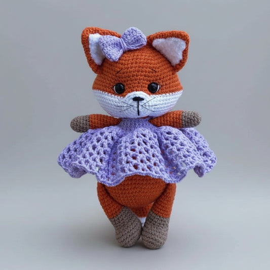 Crocheted fox amigurumi in orange and purple, wearing a lacy skirt and bow