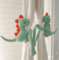 Two crocheted green and orange dinosaurs hanging on white curtains, playfully posed together.