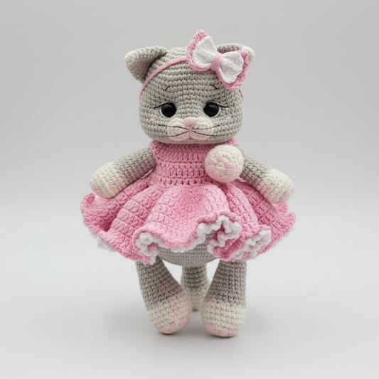 Crocheted gray cat in pink dress with bow, handmade amigurumi toy on white background