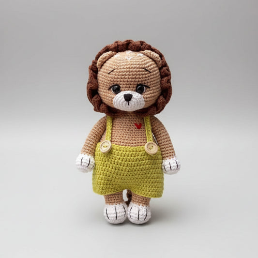 Crocheted lion stuffed animal wearing yellow overalls on a gray background