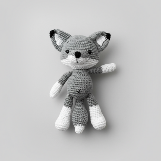 Crocheted gray and white fox stuffed animal on plain background