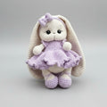 Crocheted bunny in lavender dress with bow, sitting against neutral background
