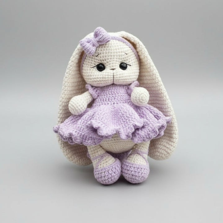 Crocheted bunny in lavender dress with bow, sitting against neutral background