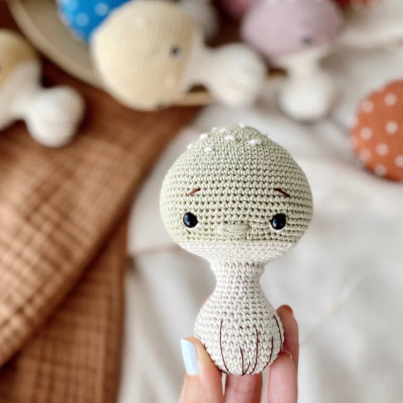Crocheted round doll with black button eyes, held by a hand with light blue nail polish