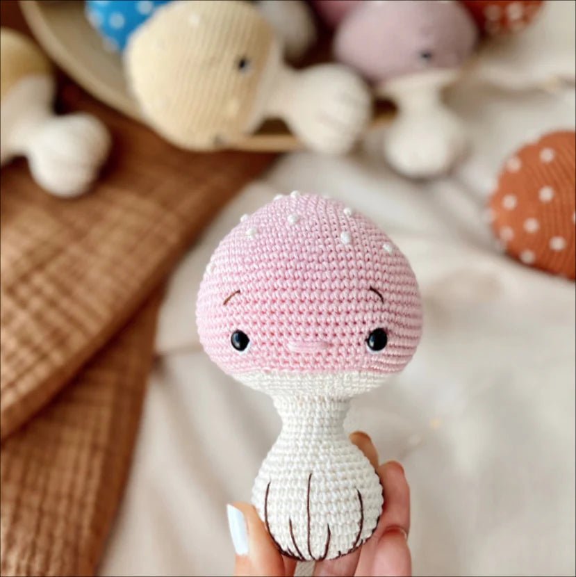 Crocheted pink and white amigurumi doll with cute button eyes, held by a hand.