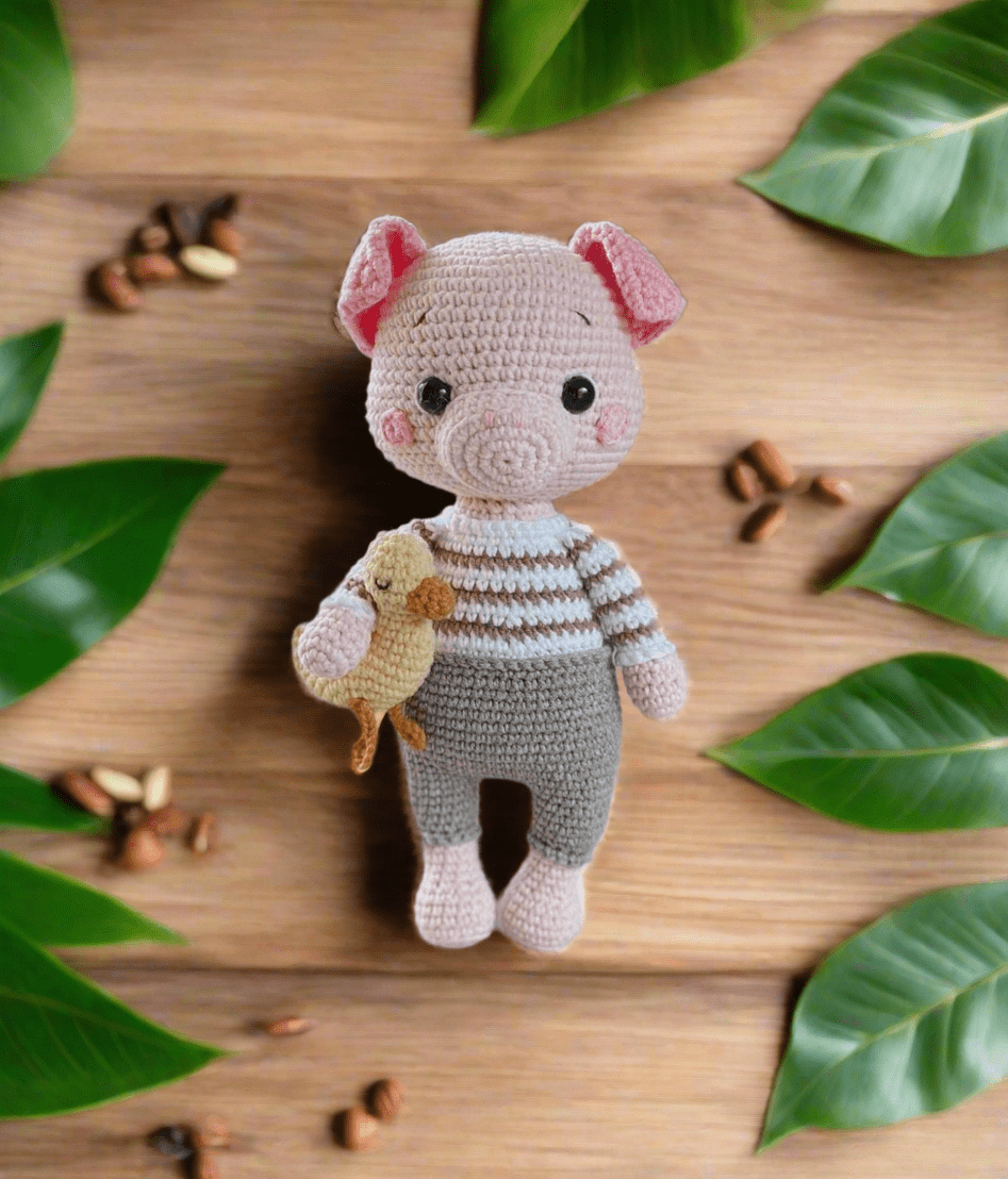 Crocheted pig plushie in striped sweater, holding a small yellow bird, surrounded by green leaves