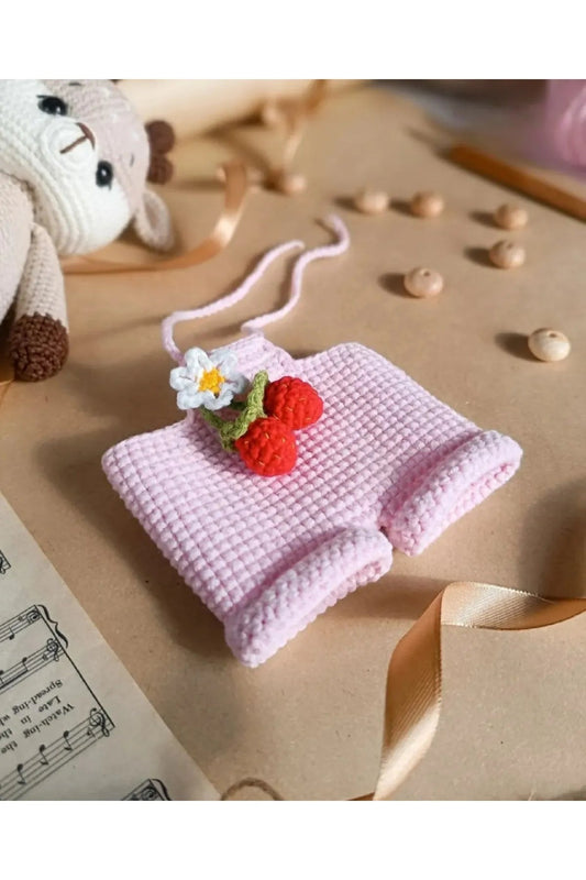 Crocheted pink cloth with miniature red strawberries and white flower, stuffed bunny nearby