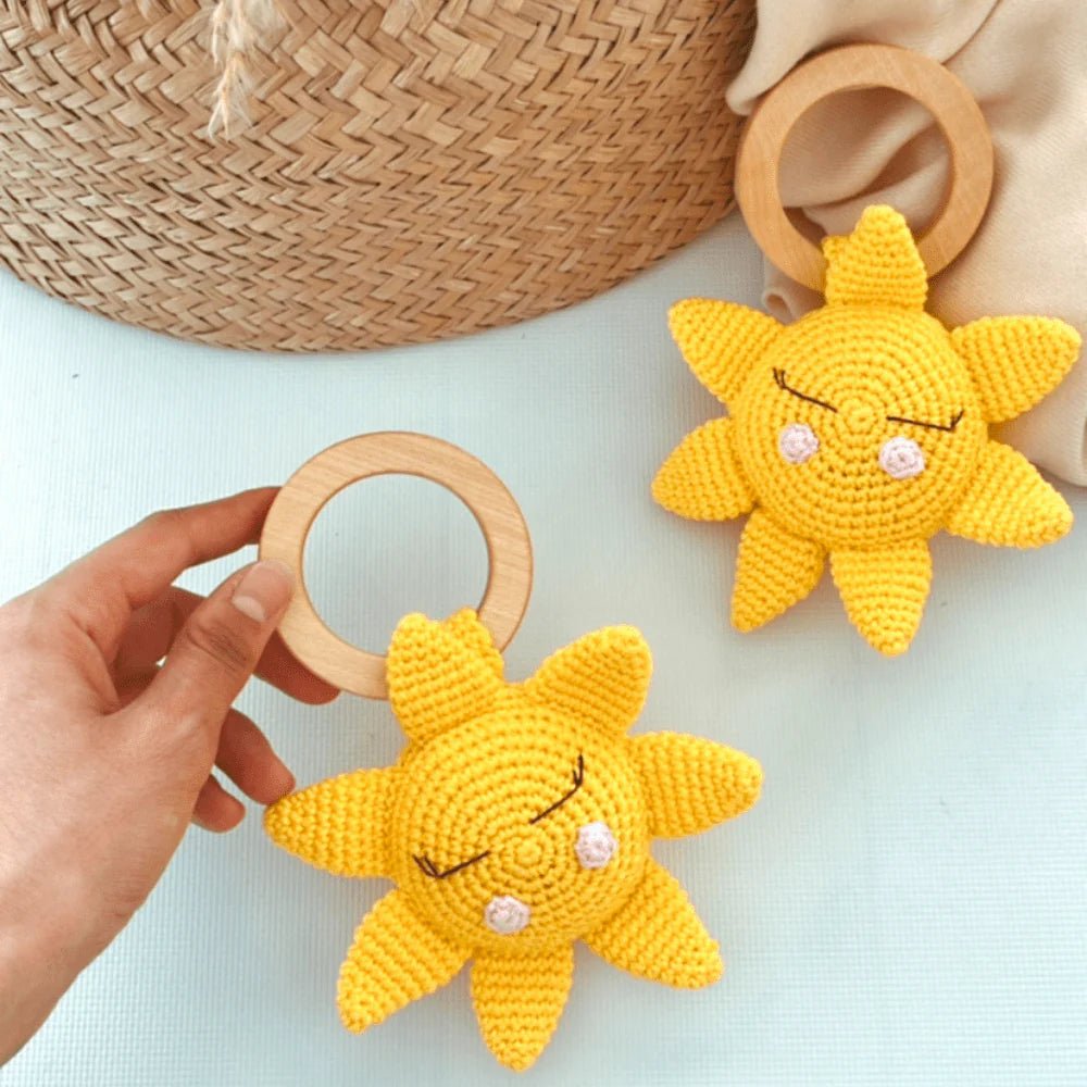 Yellow crocheted sun-shaped baby teething toys with wooden rings on light background
