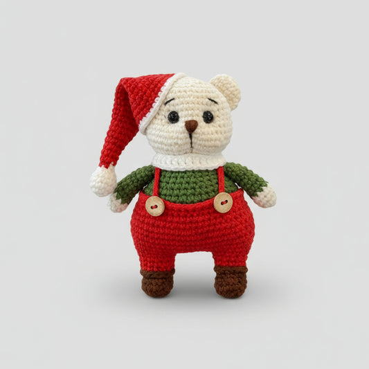 Crocheted teddy bear in Christmas outfit with Santa hat and red overalls