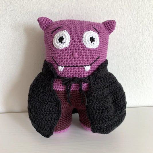 Crocheted purple monster plush with big eyes and sharp teeth, wearing a black jacket