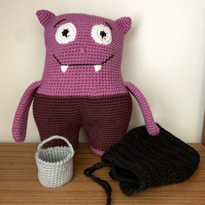Purple crocheted monster plush with fangs, next to small basket and black yarn